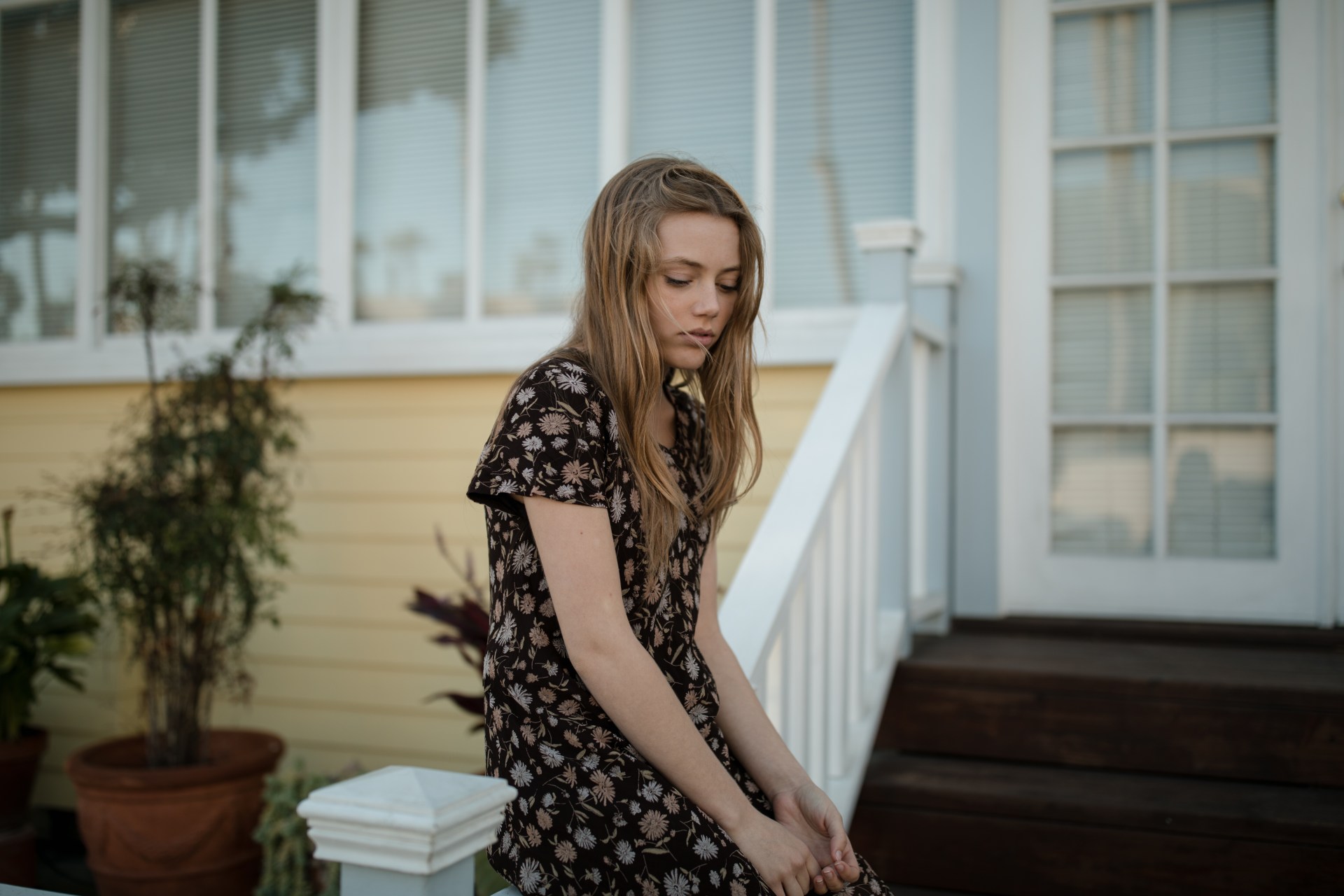 woman sitting on front railing of house looking sad