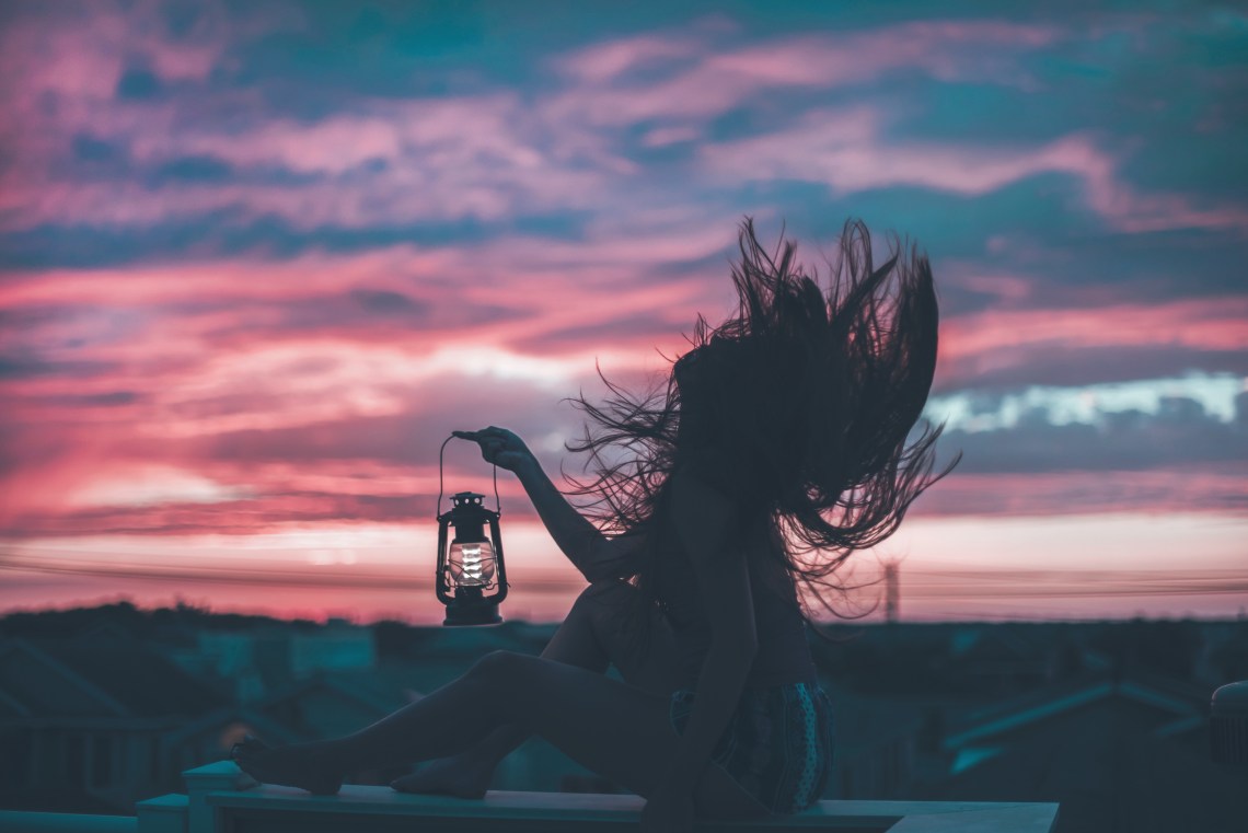 woman holding vintage lantern at sunrise