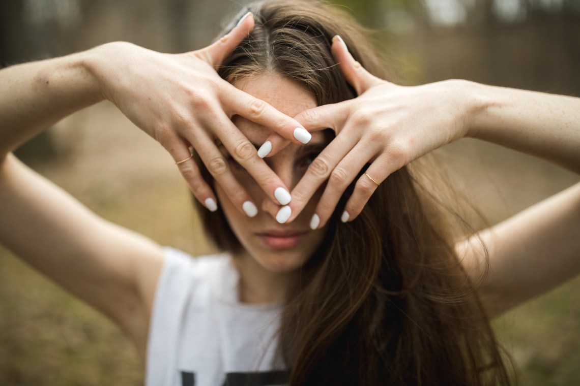woman covering face wearing white nail polish