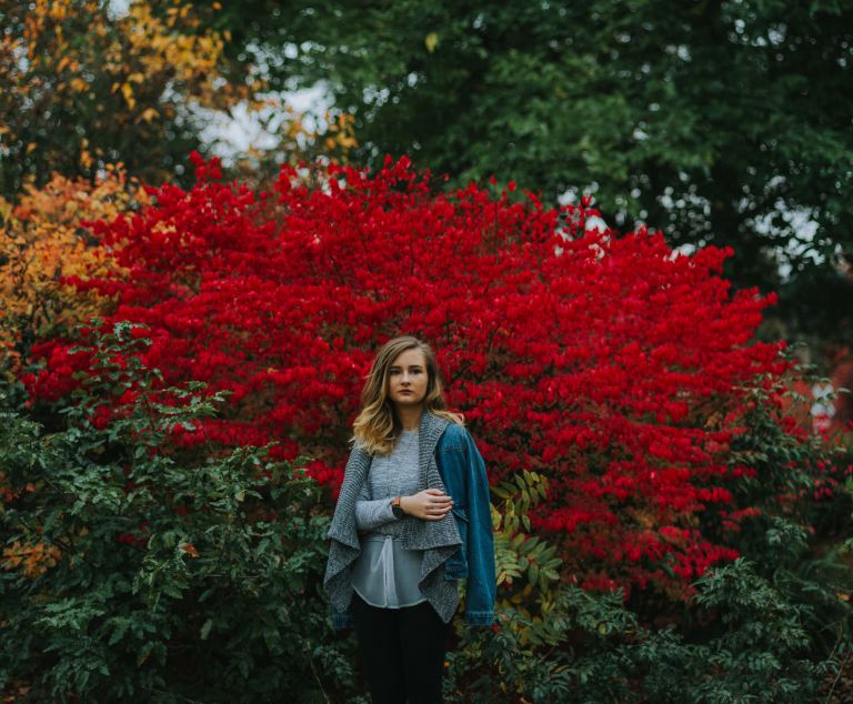 woman in blue cardigan standing near red petaled flowers