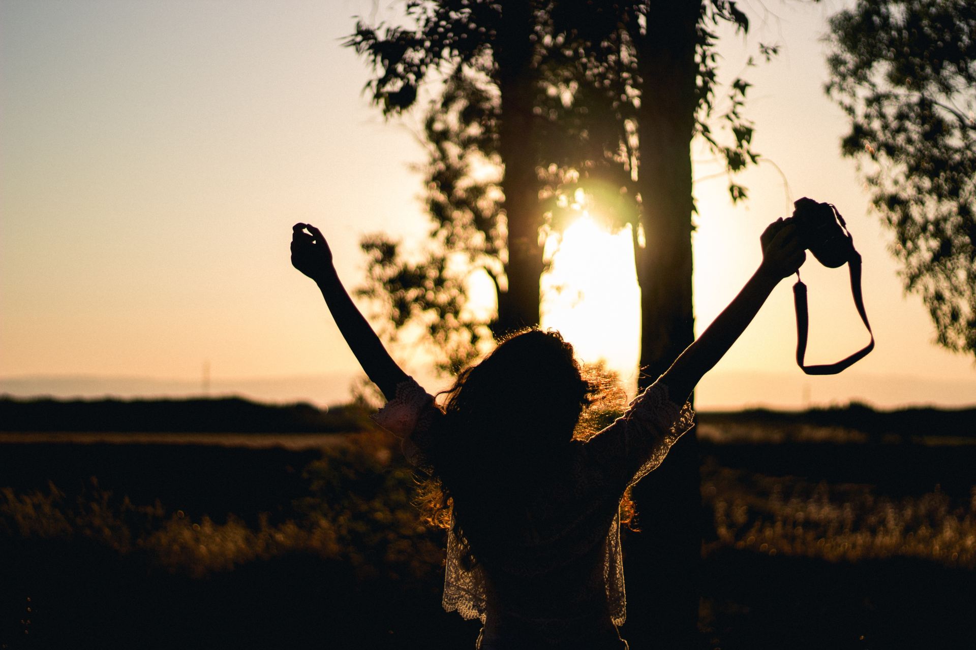 silhouette photo of woman raising her hands while holding DSLR camera