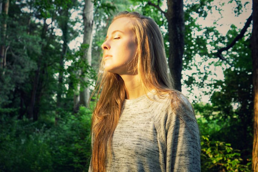 woman in gray long sleeve shirt standing near green trees during daytime