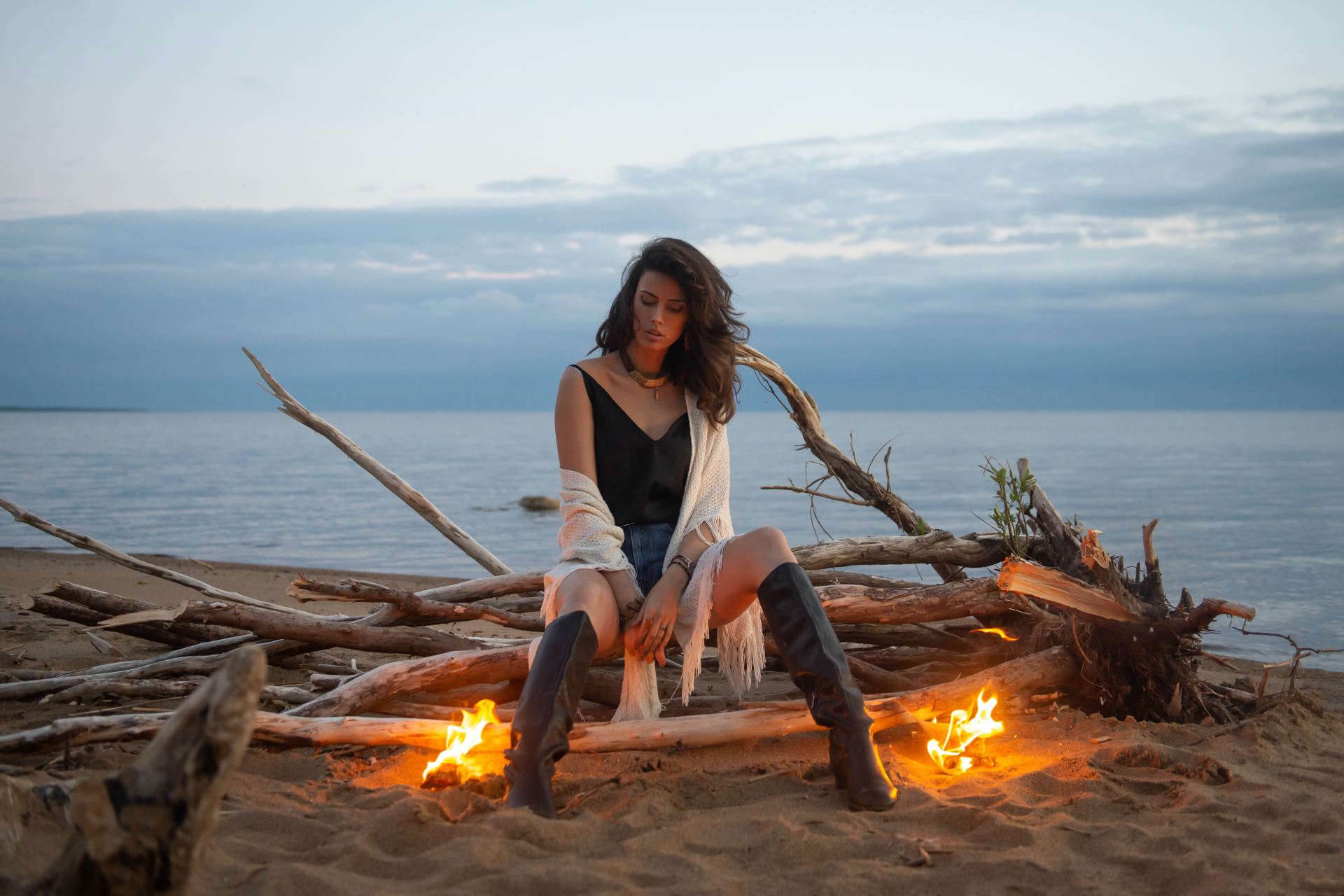 woman in white tank top sitting on brown log near bonfire during daytime