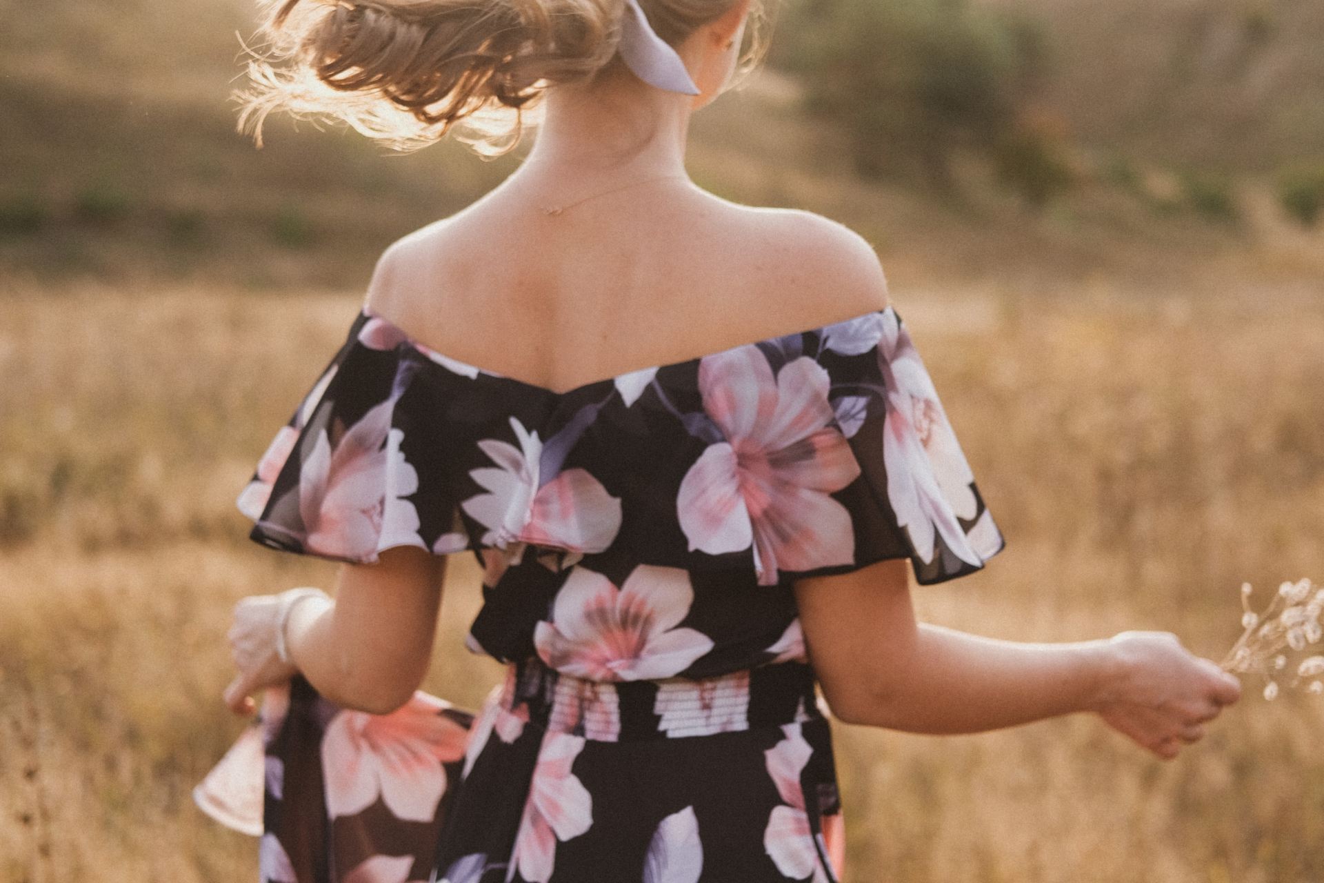 girl in black and pink floral dress standing on brown grass field during daytime