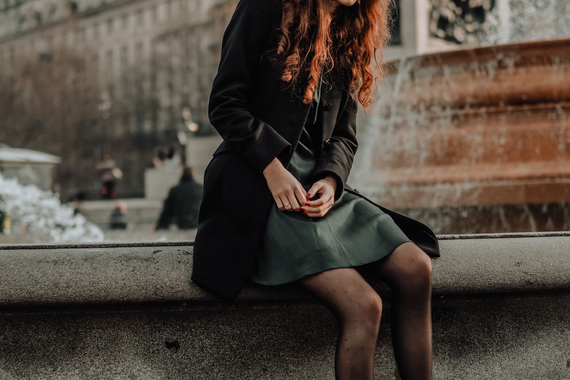 woman in black long sleeve dress sitting on gray concrete bench during daytime