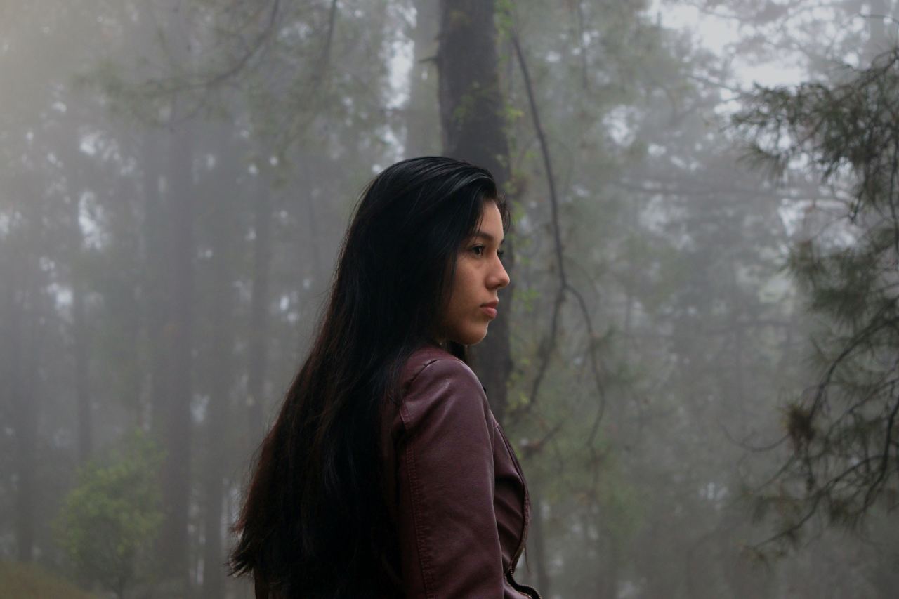 woman in brown jacket standing near trees during daytime