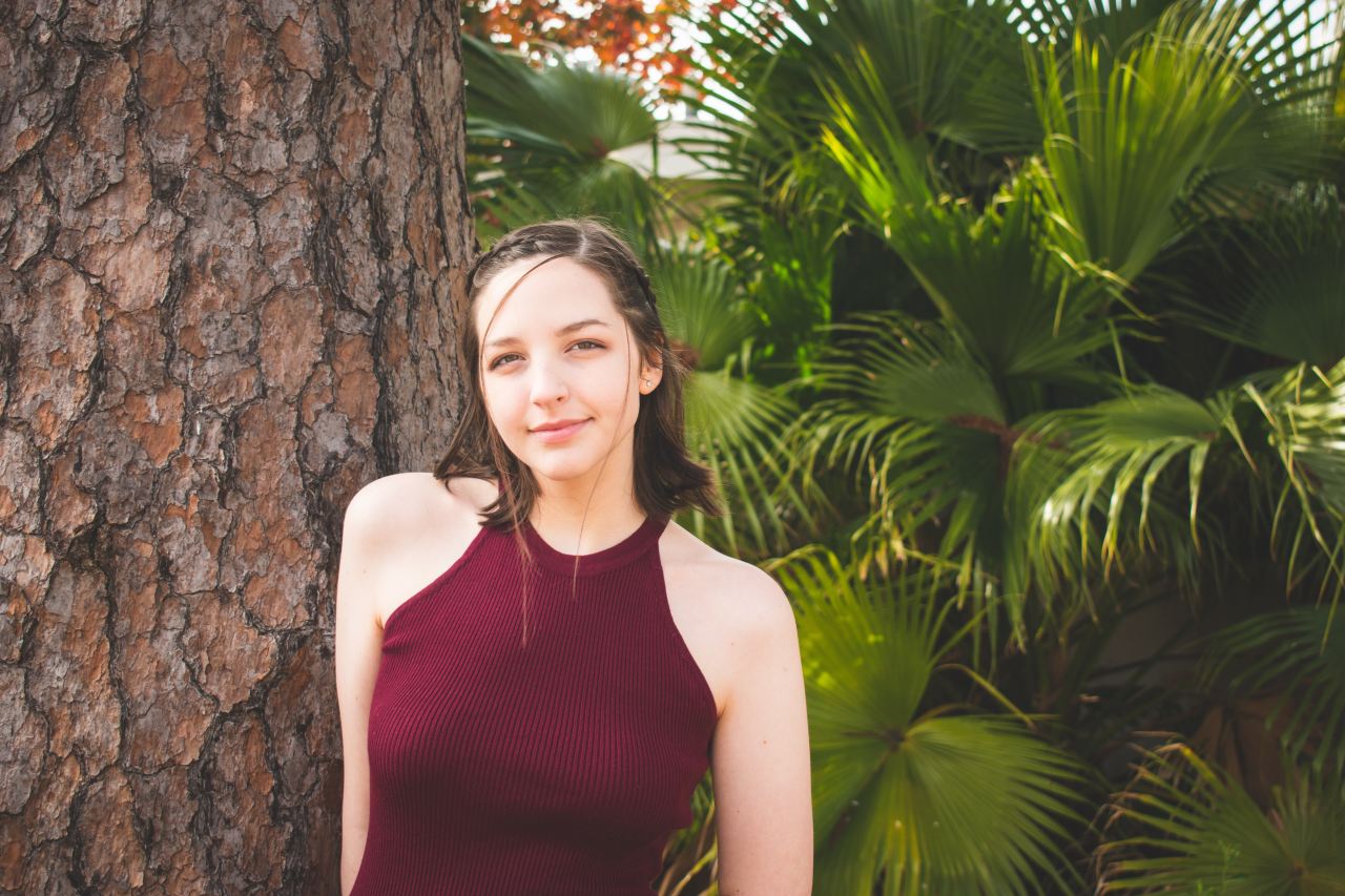 woman in red tank top standing beside brown tree