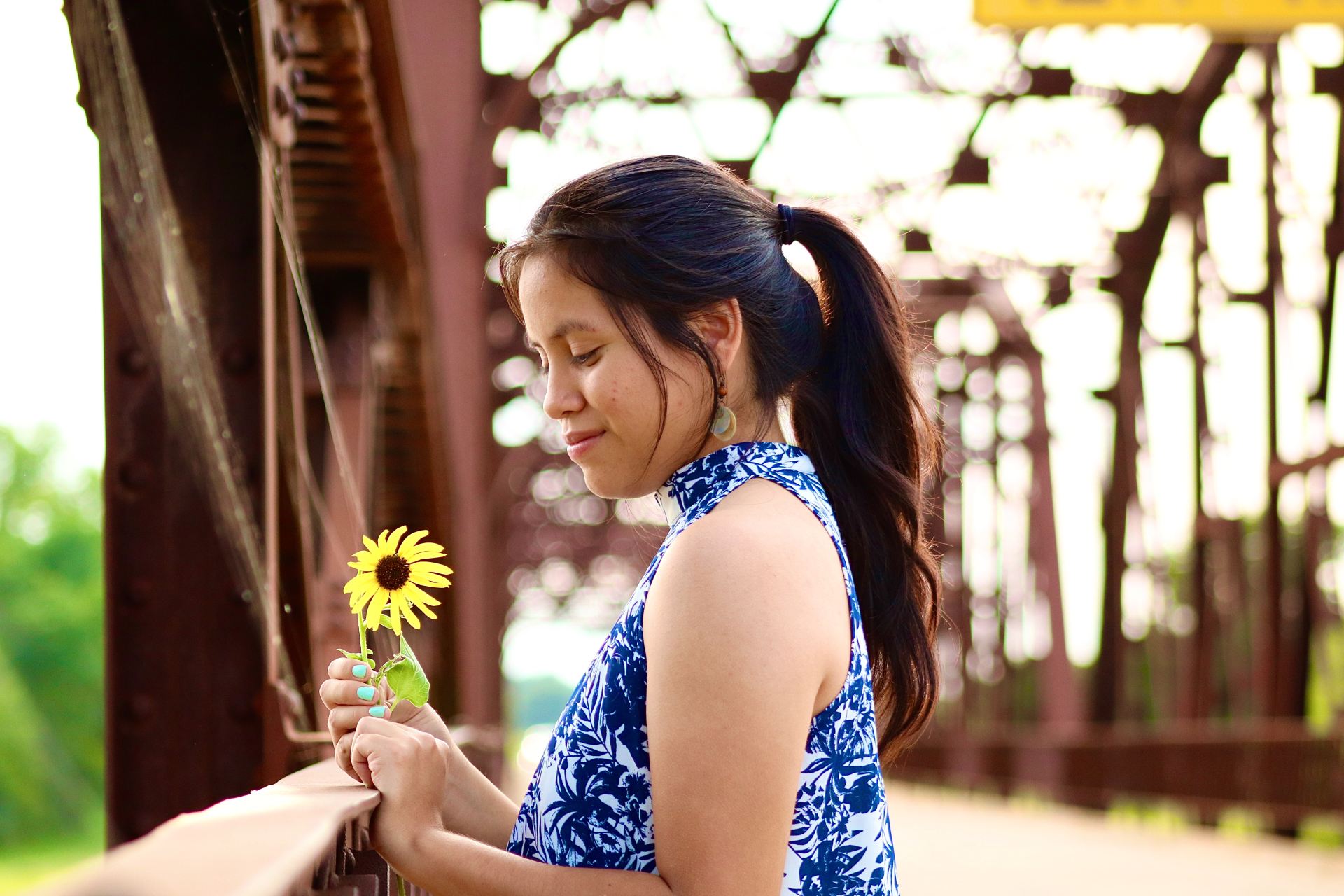 woman in blue and white floral sleeveless dress holding yellow flower during daytime