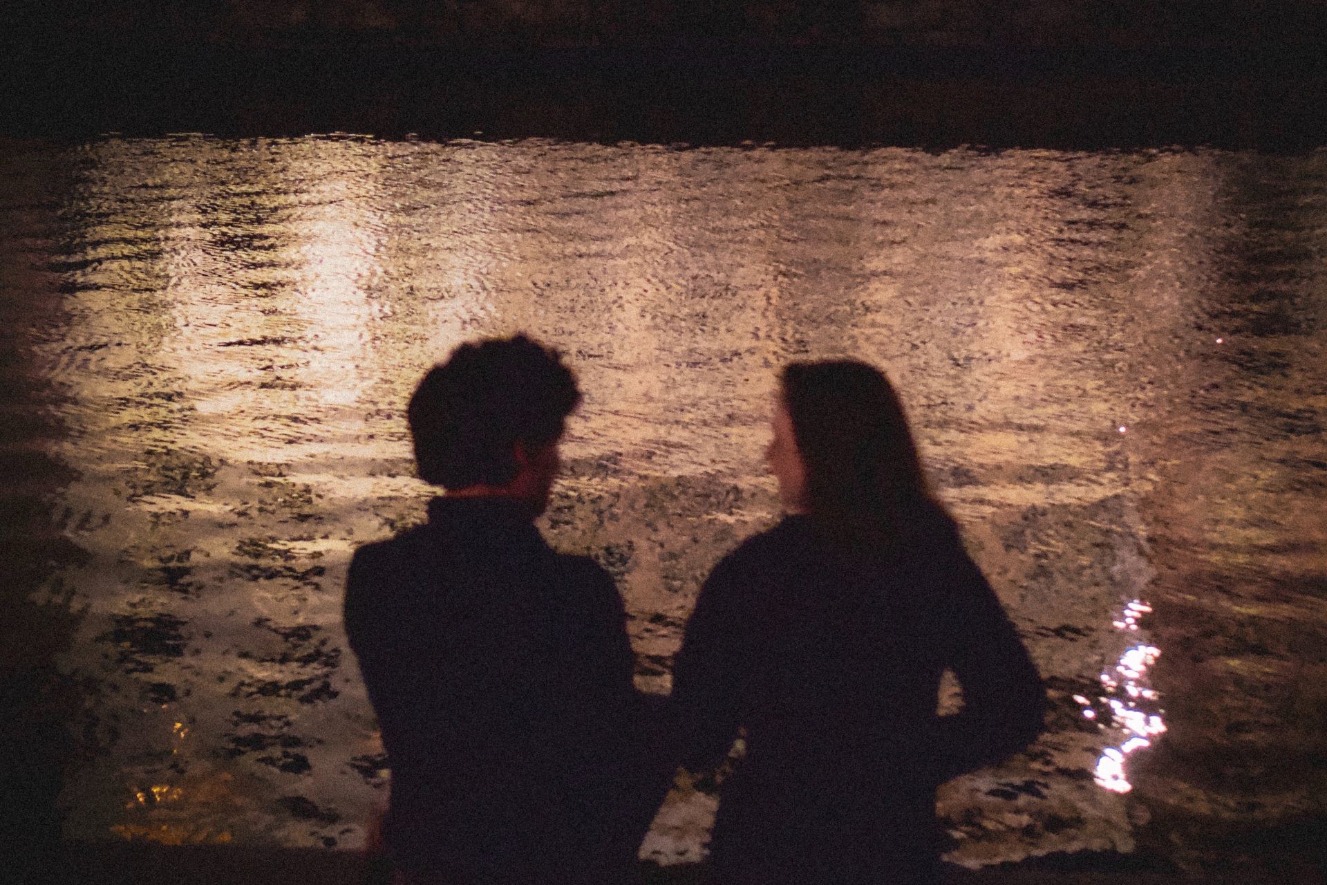 silhouette of man and woman standing beside body of water during night time