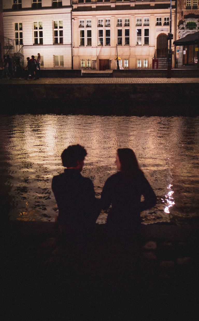 silhouette of man and woman standing beside body of water during night time