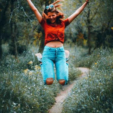 woman in orange t-shirt and blue denim jeans standing on green grass field during daytime