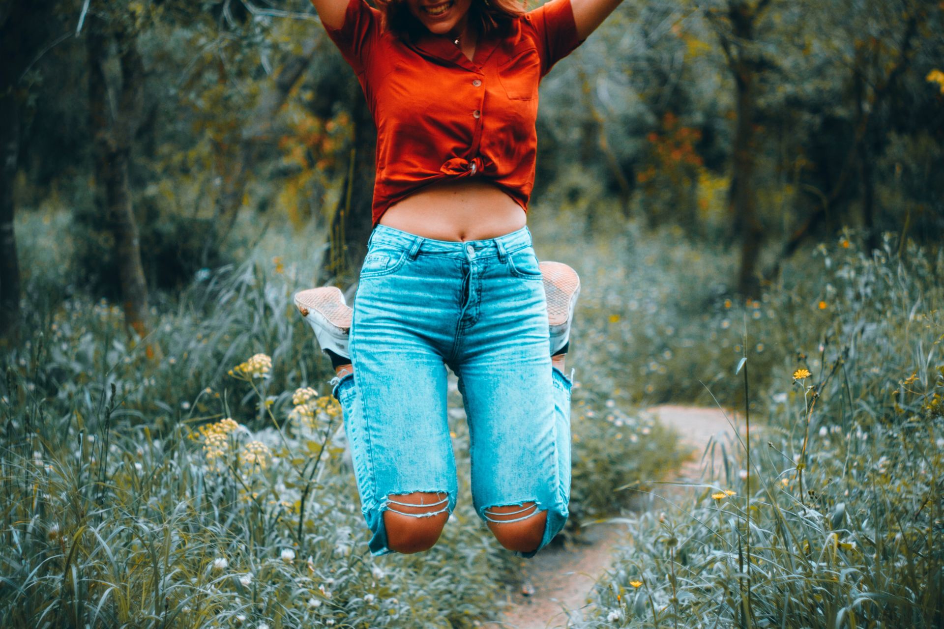 woman in orange t-shirt and blue denim jeans standing on green grass field during daytime