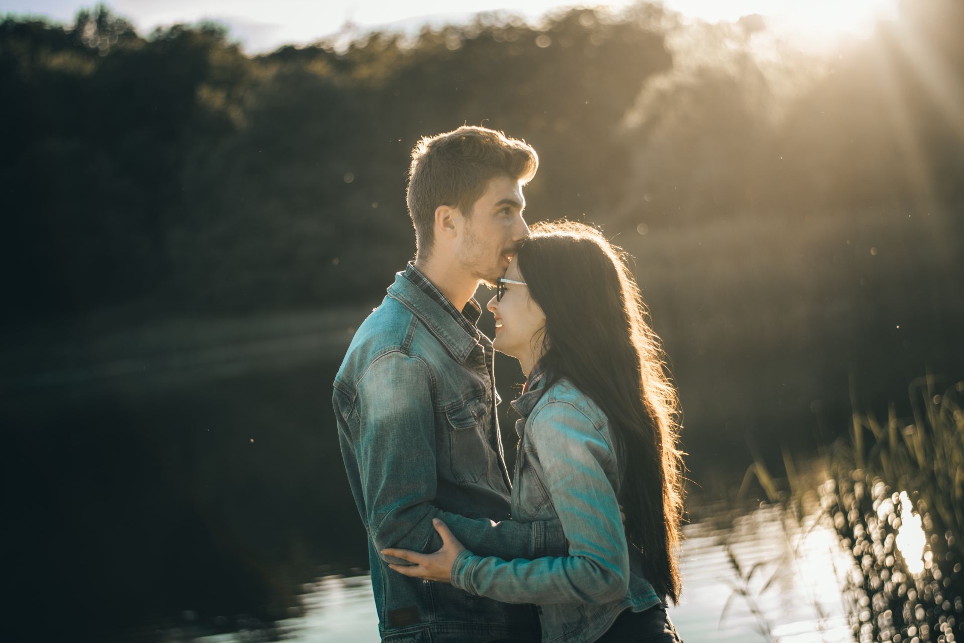 man kissing woman's forehead in front of lake