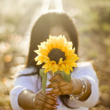 woman holding up sunflower outdoor during daytime