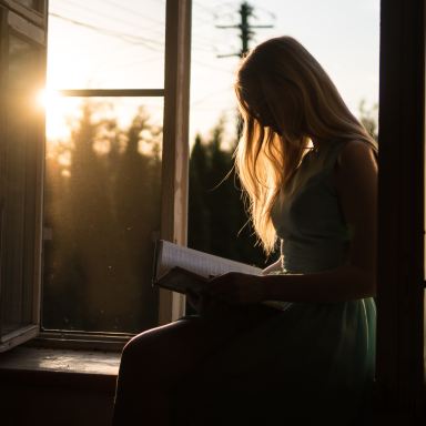 woman reading book while sitting at window