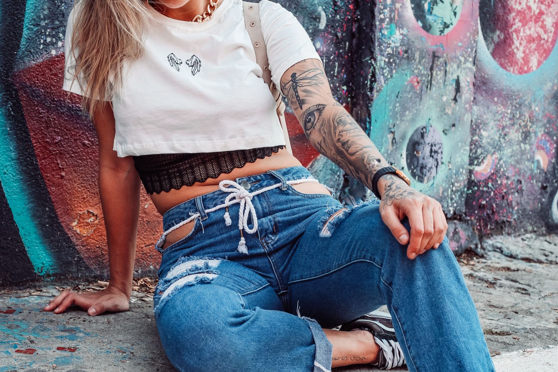 woman in white long sleeve shirt and blue denim jeans sitting on concrete wall during daytime