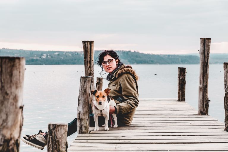 woman sitting on brown wooden dock with dog