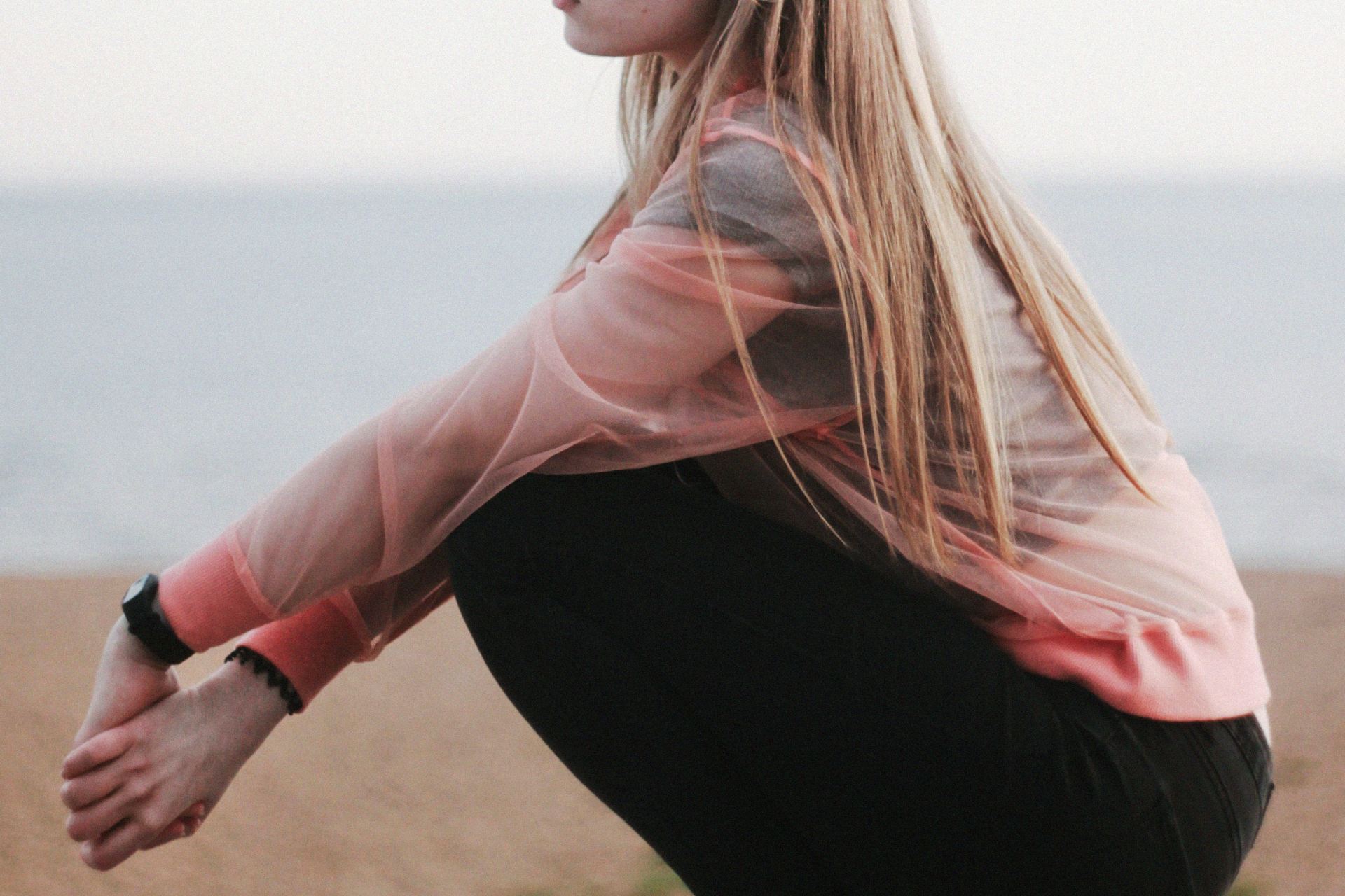 woman in pink long sleeve shirt and black pants sitting on brown sand during daytime