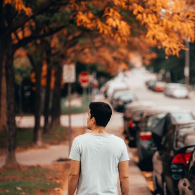 man wearing white shirt walking near vehicles and tree