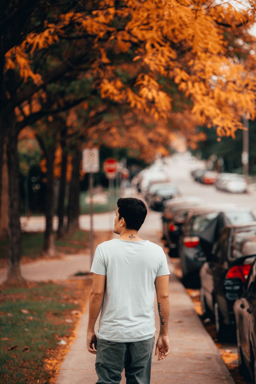 man wearing white shirt walking near vehicles and tree