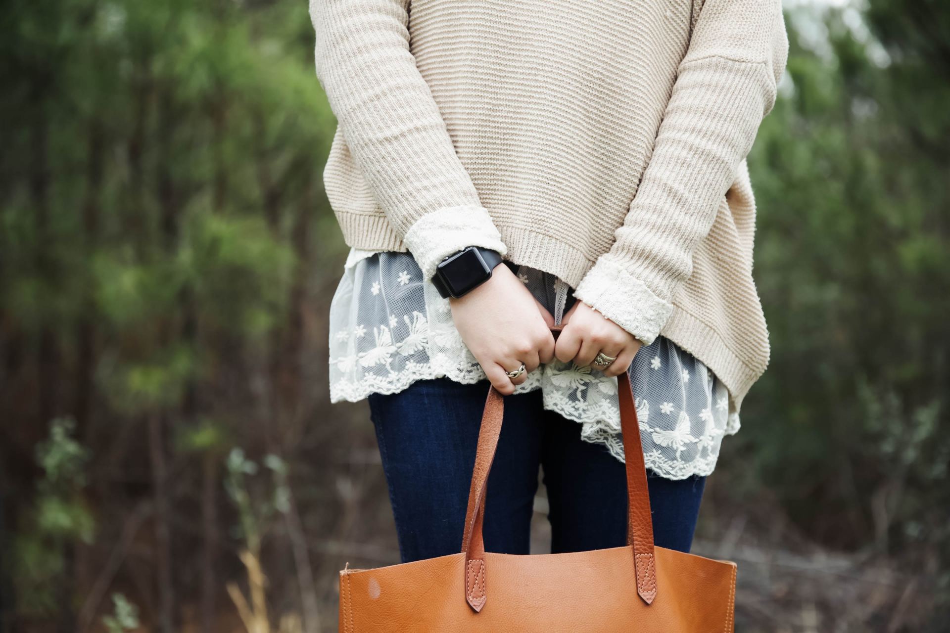 woman standing holding a brown leather tote bag