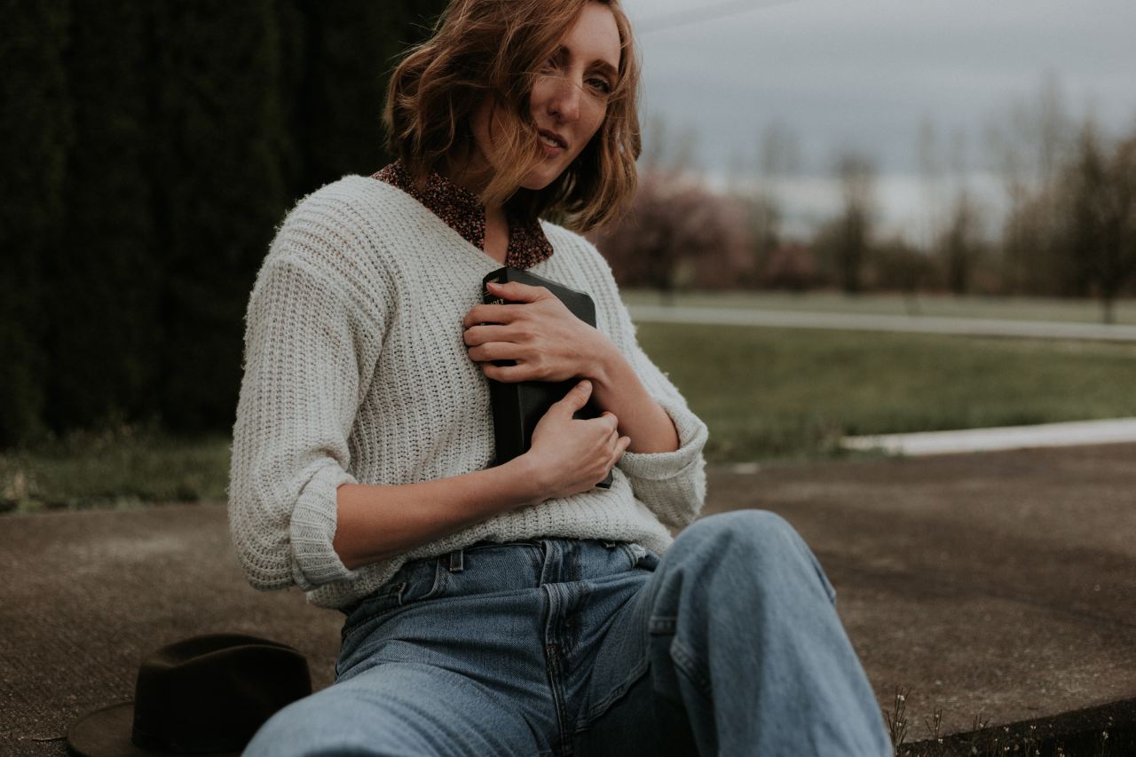 woman carrying black bag while sitting on brown concrete pathway