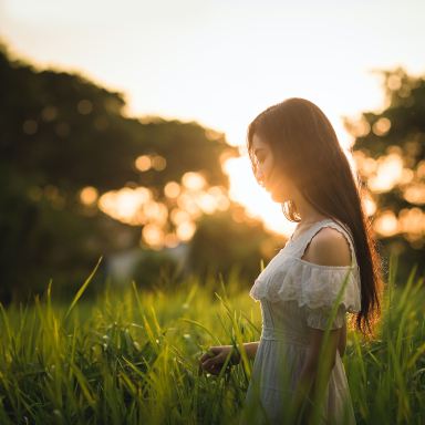 shallow focus photography of woman standing on grass field while holding grass