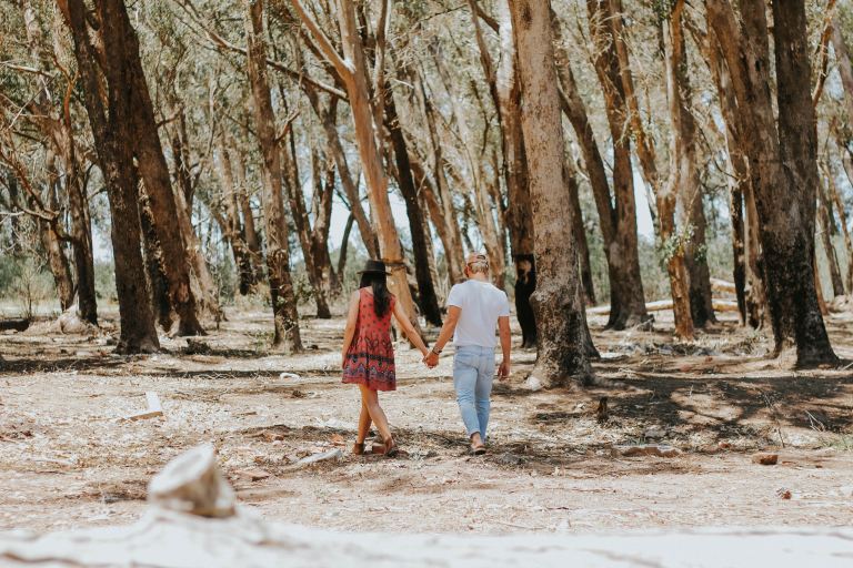 man and woman holding hands while walking under tree