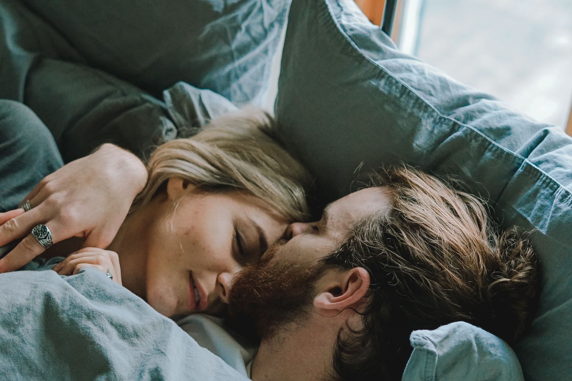 man kissing woman's forehead while lying on bed