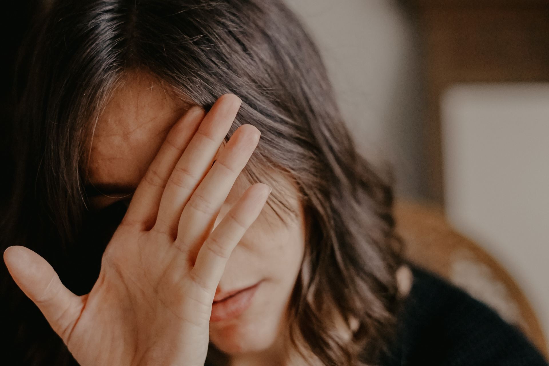 woman in black blazer covering her face