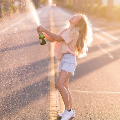 woman in white shirt and blue denim shorts holding green bottle standing on road during daytime