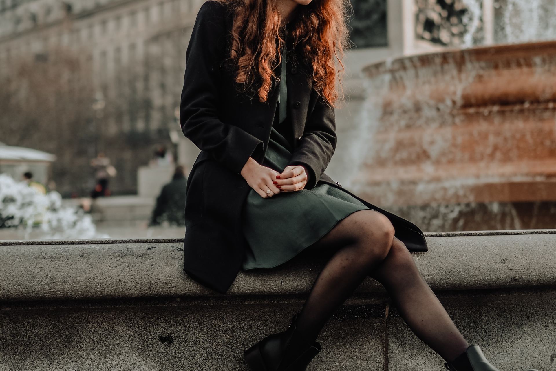 woman in black coat sitting on concrete bench during daytime