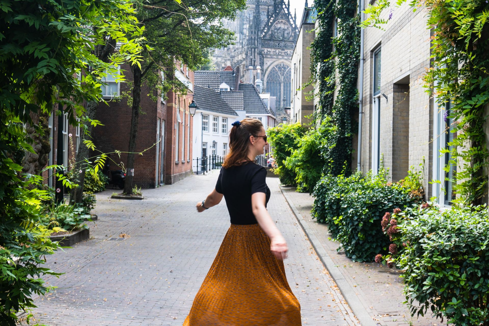 woman in black long sleeve shirt and red skirt walking on sidewalk during daytime