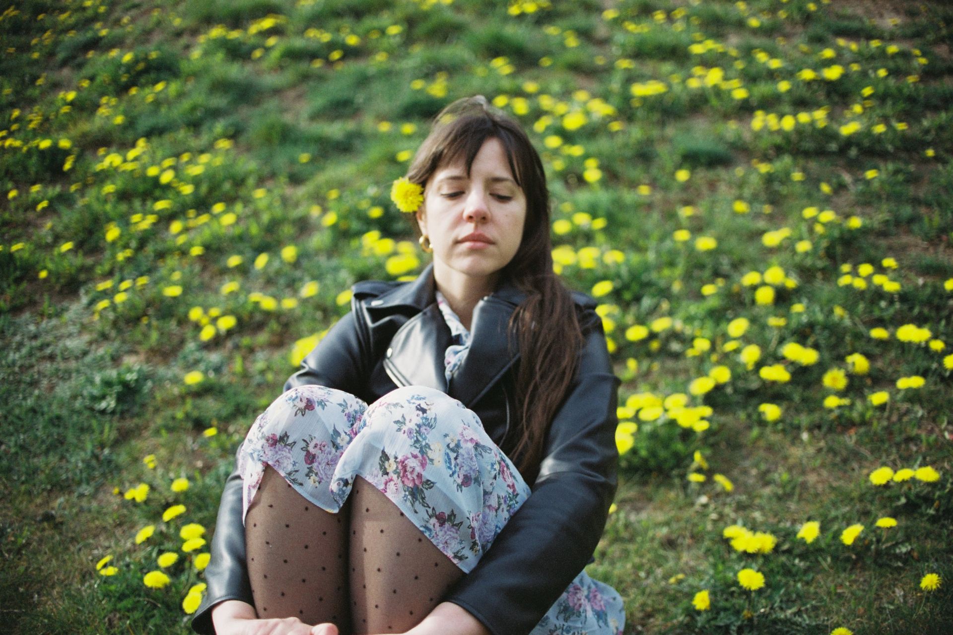 woman in black jacket sitting on yellow flower field during daytime