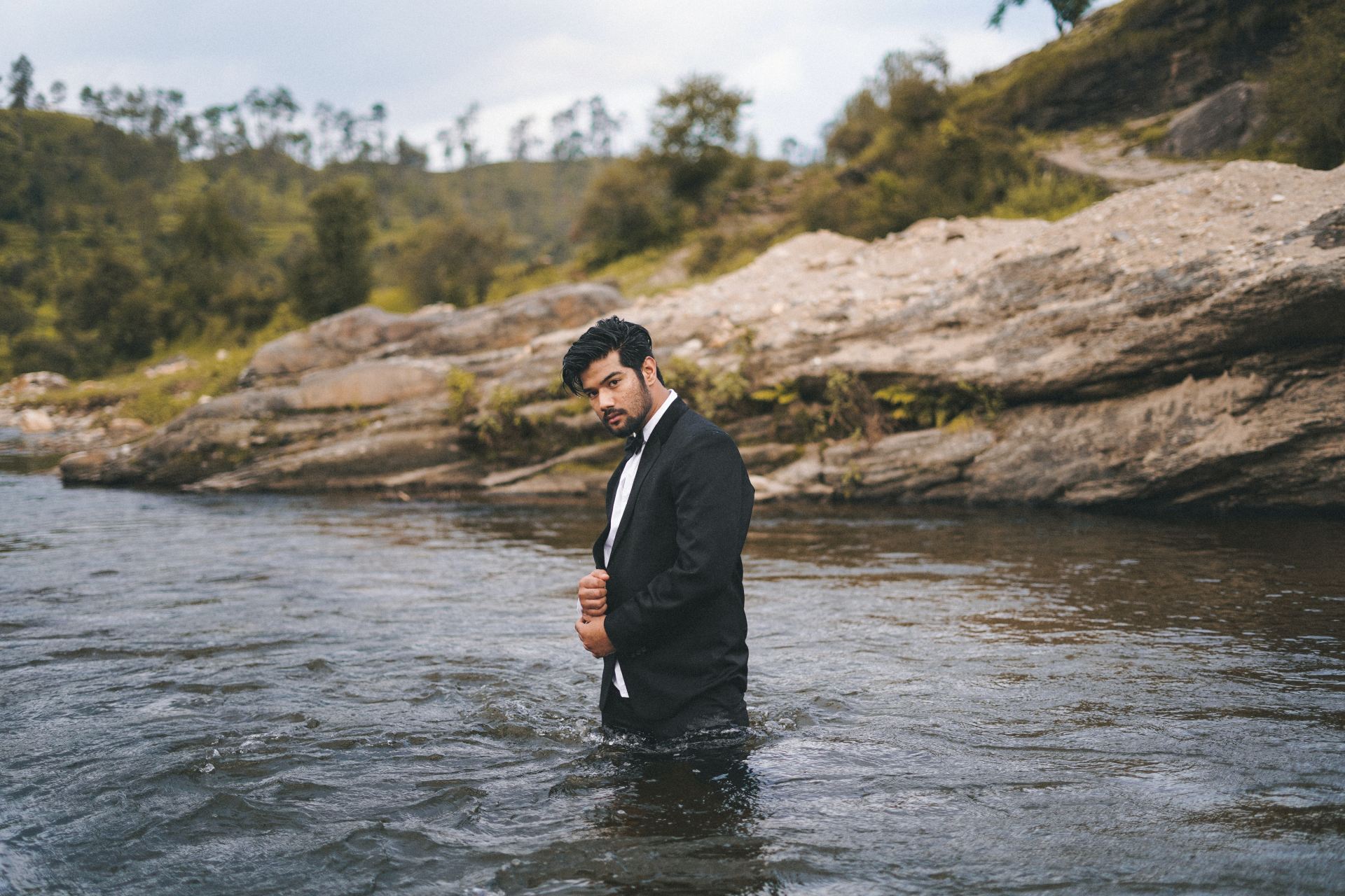 man in black suit standing on river during daytime