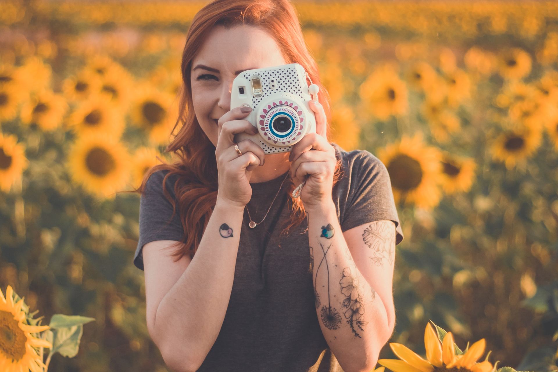 woman holding white instant camera standing on meadow of Sunflowers