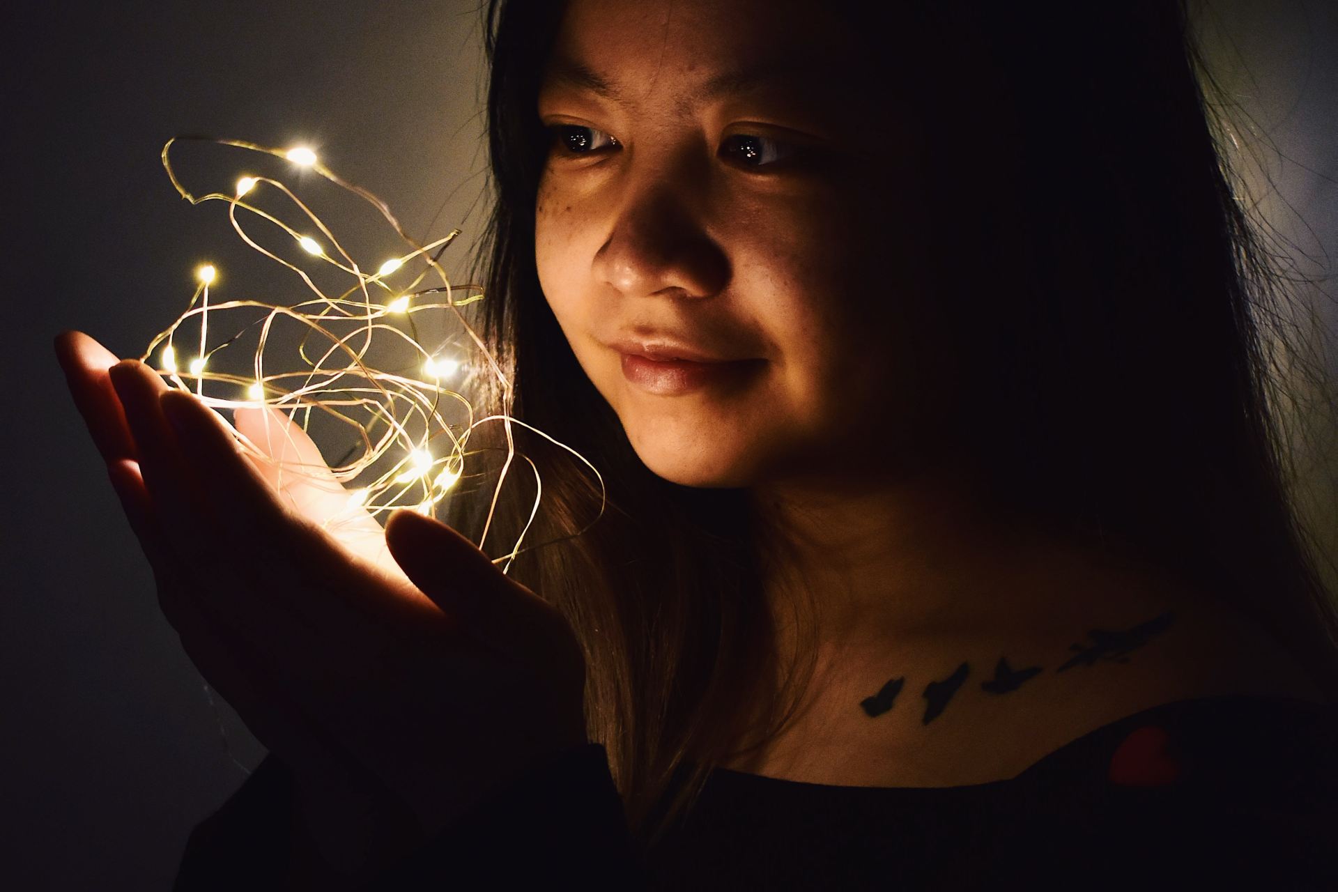 woman holding string lights in dark room