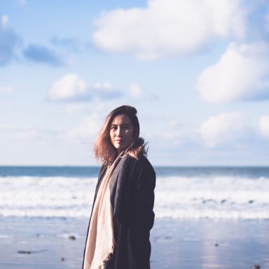 woman in black coat standing on beach during daytime