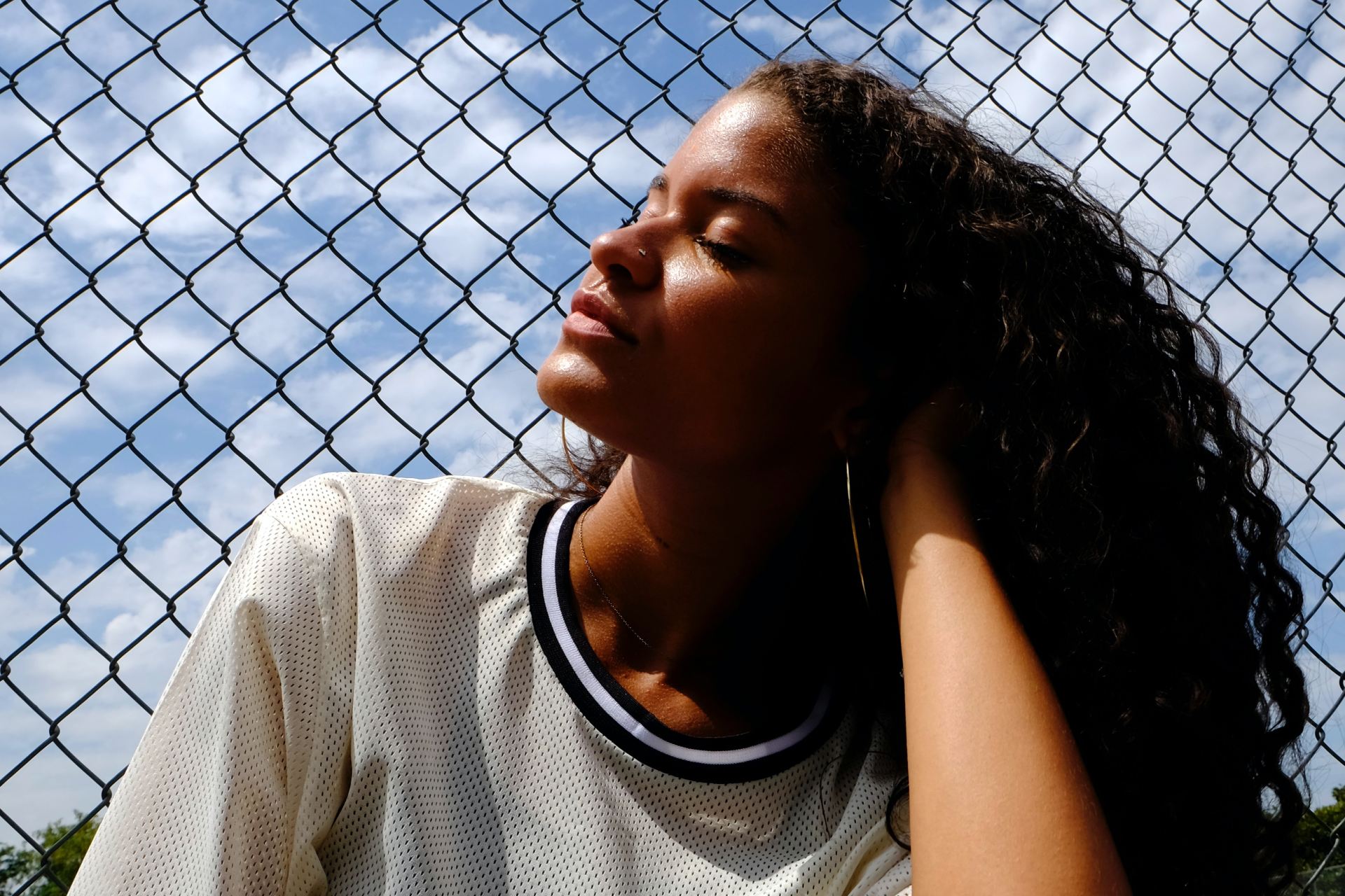 woman in white crew neck t-shirt leaning on chain link fence