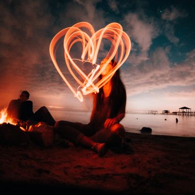 woman sitting on sand near bonfire