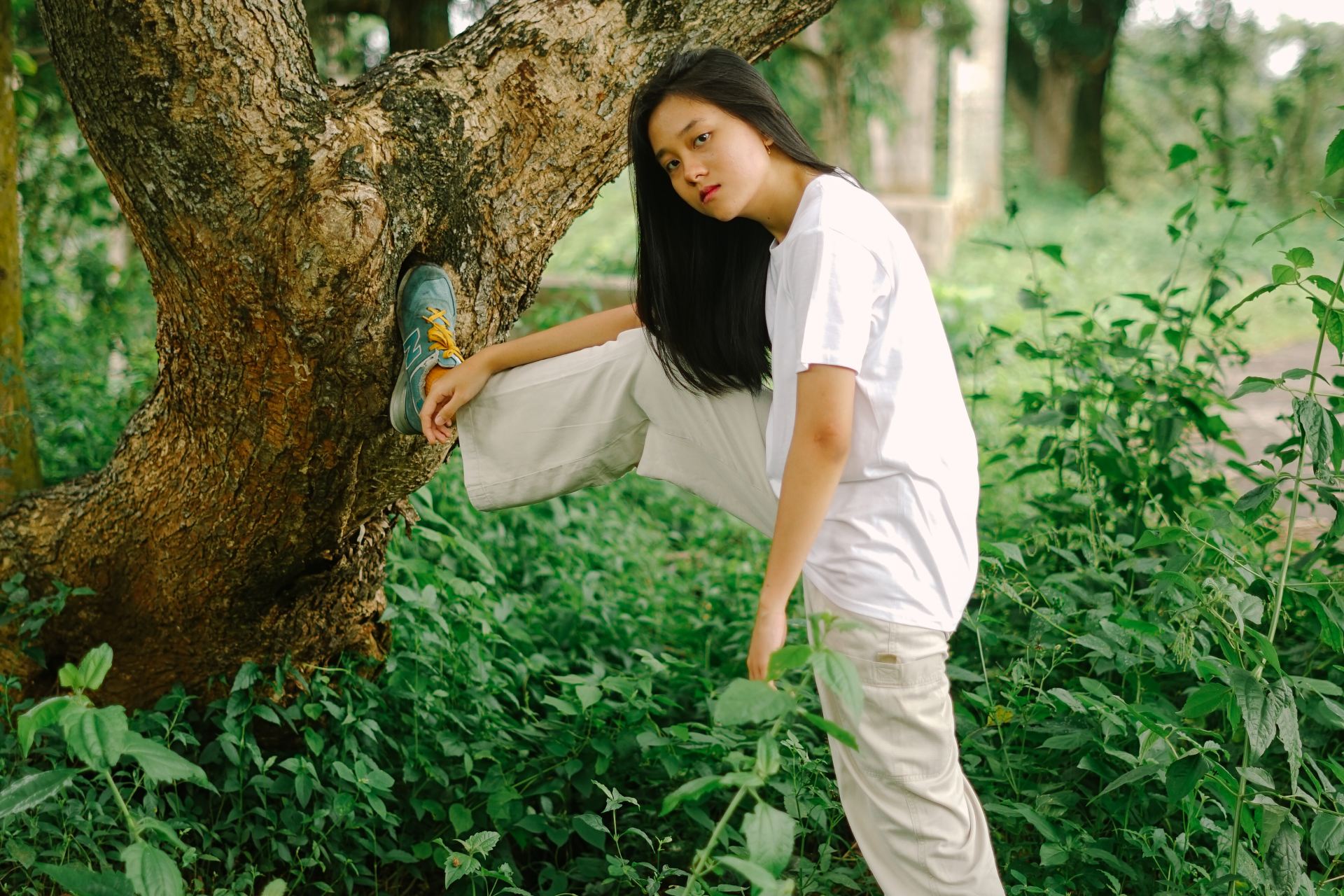 woman in white shirt and white pants standing beside tree