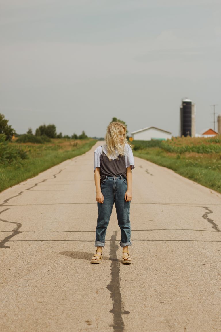 woman in white t-shirt and blue denim jeans walking on gray concrete road during daytime