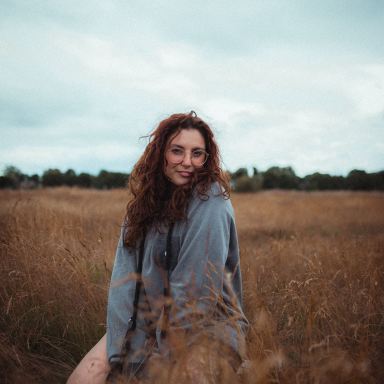 woman in blue long sleeve shirt sitting on brown grass field during daytime