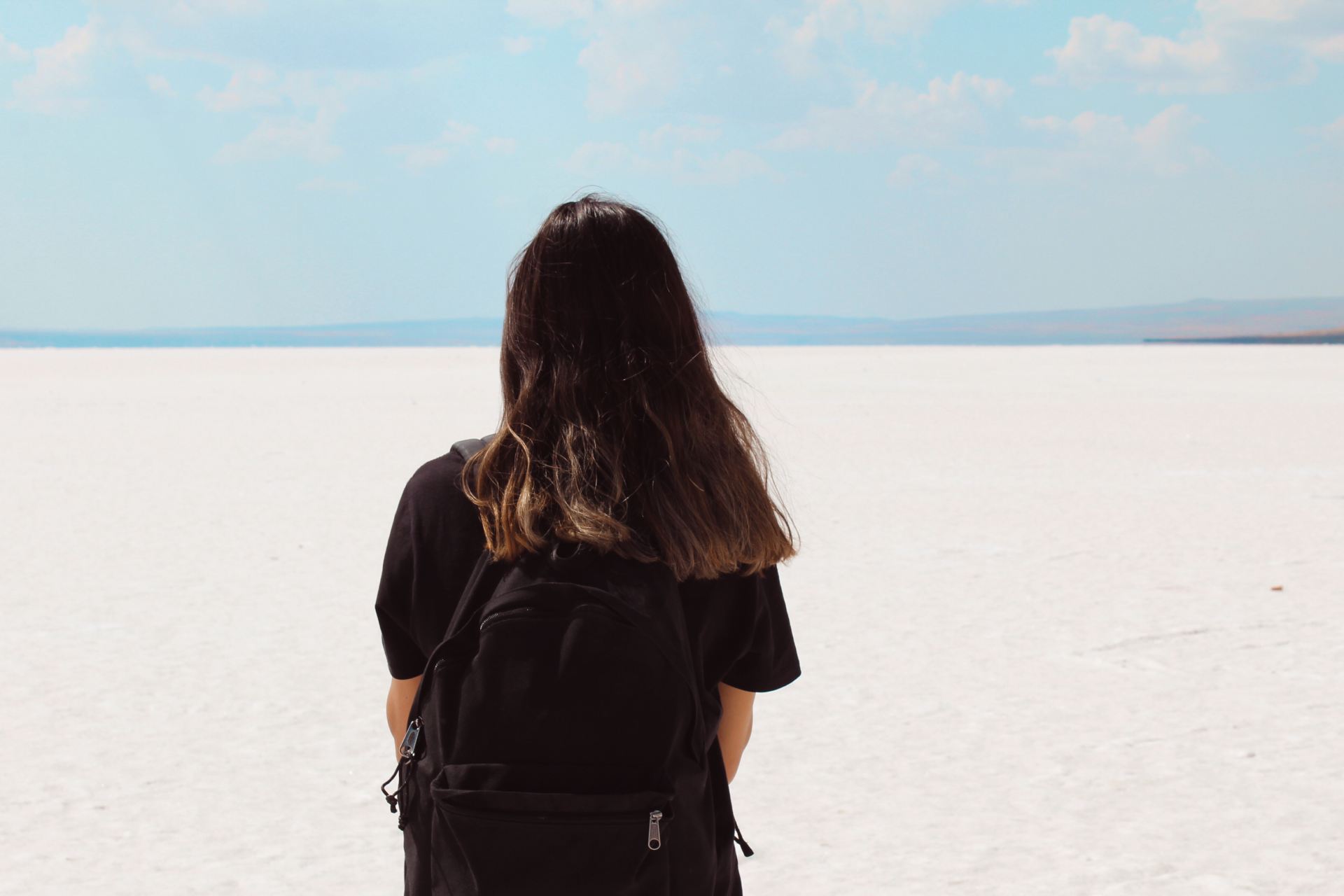 woman facing white field with backpack at daytime