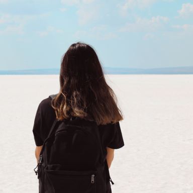 woman facing white field with backpack at daytime