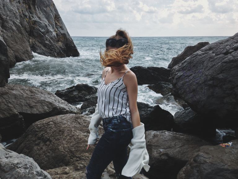 woman in white tank top and blue denim jeans standing on rocky shore during daytime